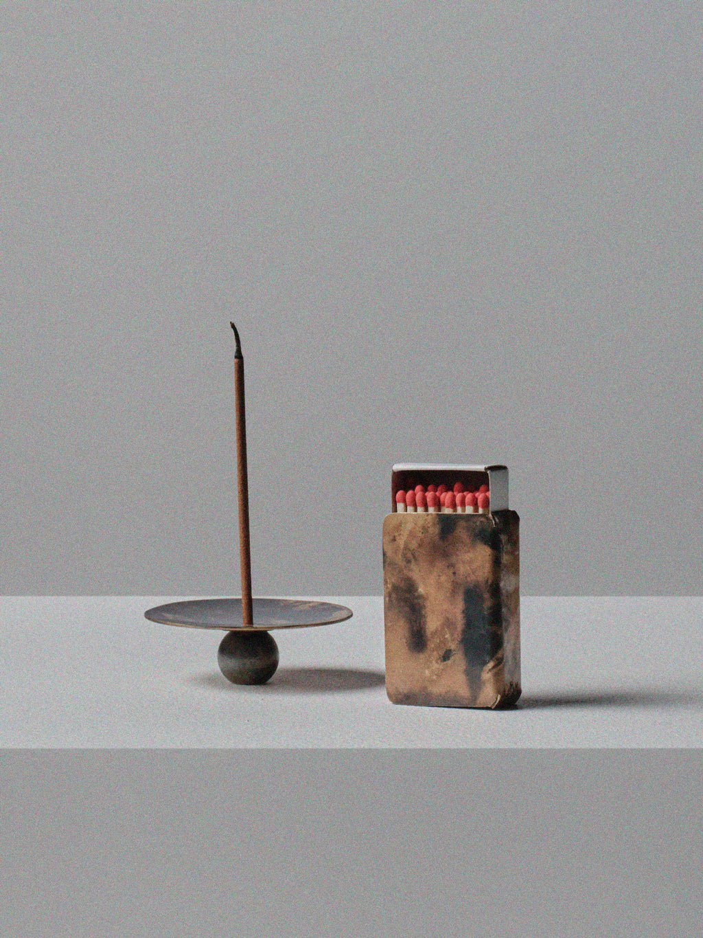Handmade brass incense holder with burning stick and patinated brass matchbox cover by 13 Knives, displayed on a minimal grey surface