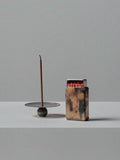 Handmade brass incense holder with burning stick and patinated brass matchbox cover by 13 Knives, displayed on a minimal grey surface