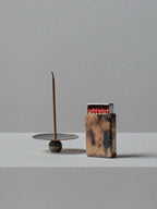 Handmade brass incense holder with burning stick and patinated brass matchbox cover by 13 Knives, displayed on a minimal grey surface