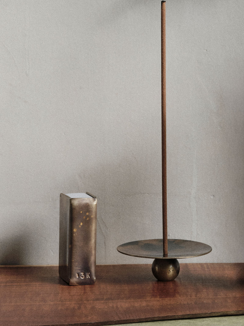13 Knives handmade brass matchbox holder and brass incense burner set shown on a timber tabletop with a burning incense stick