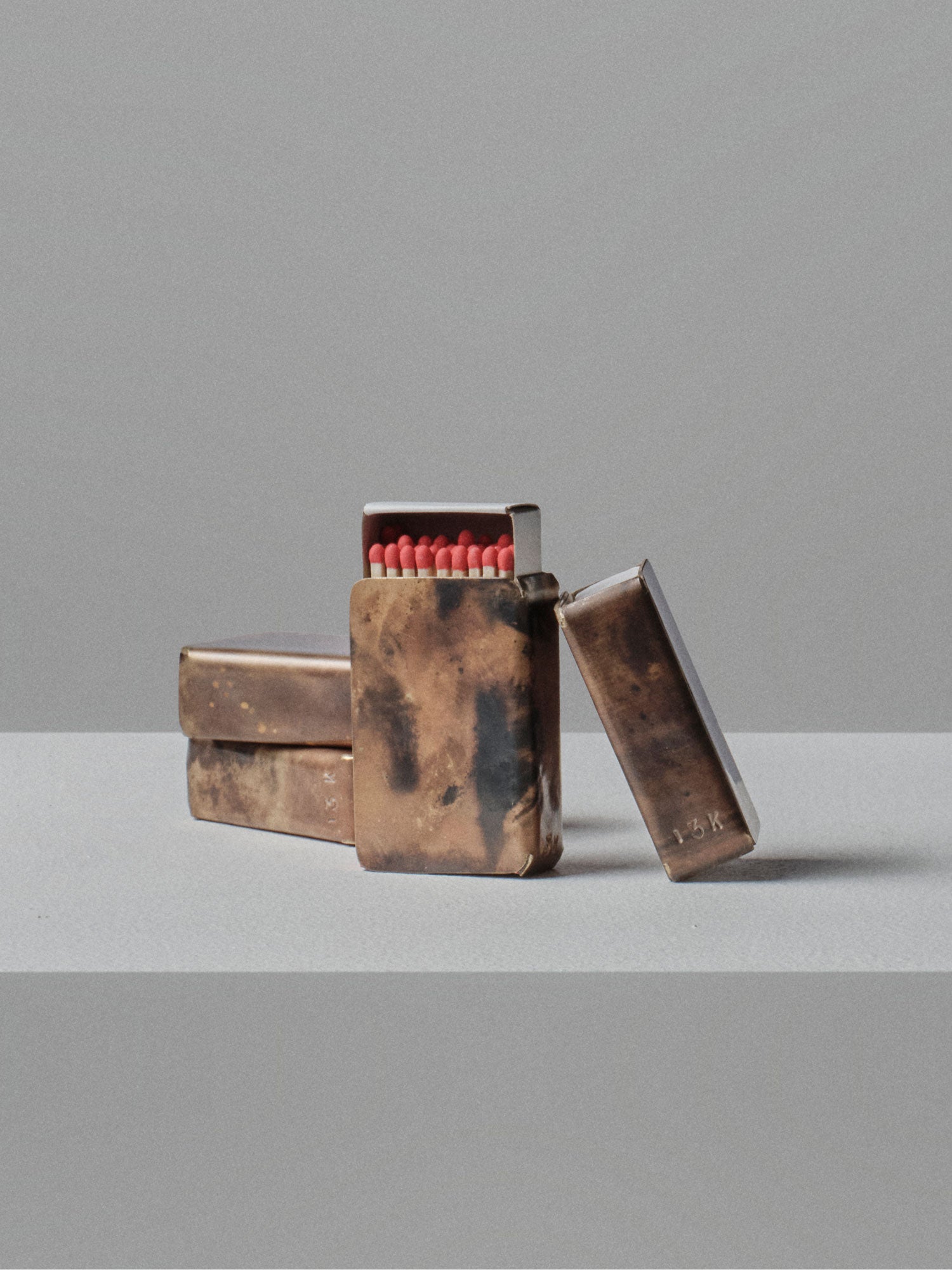 Stacked handcrafted brass matchbox holders by 13 Knives with unique flame patinas and exposed match heads