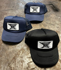 Three trucker hats in navy and black with a 13knives and cutlery anvil logo on a metal shop workbench 